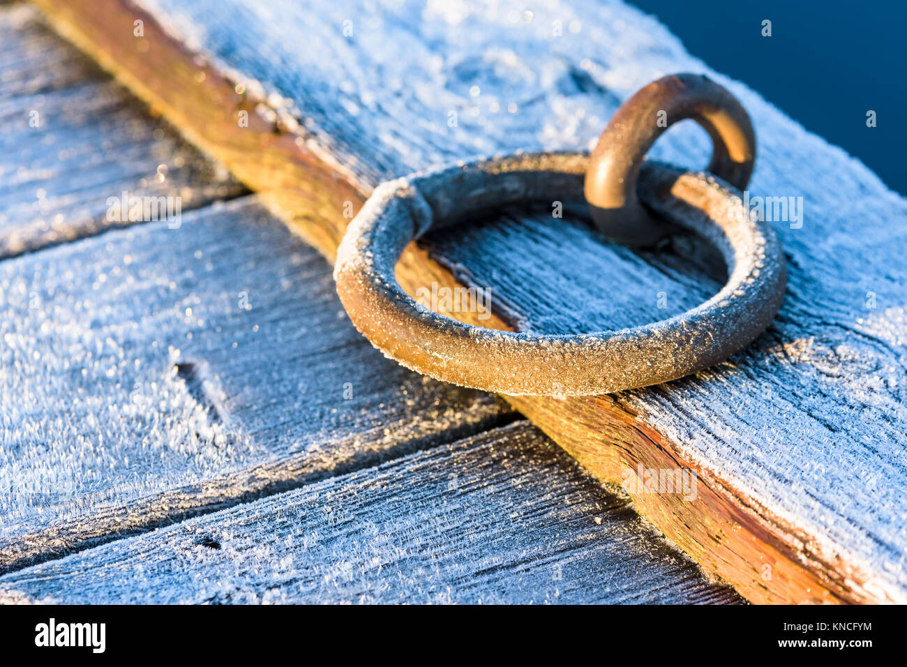 Frost covered metal mooring ring at a wooden pier on a cold morning. Stock Photo