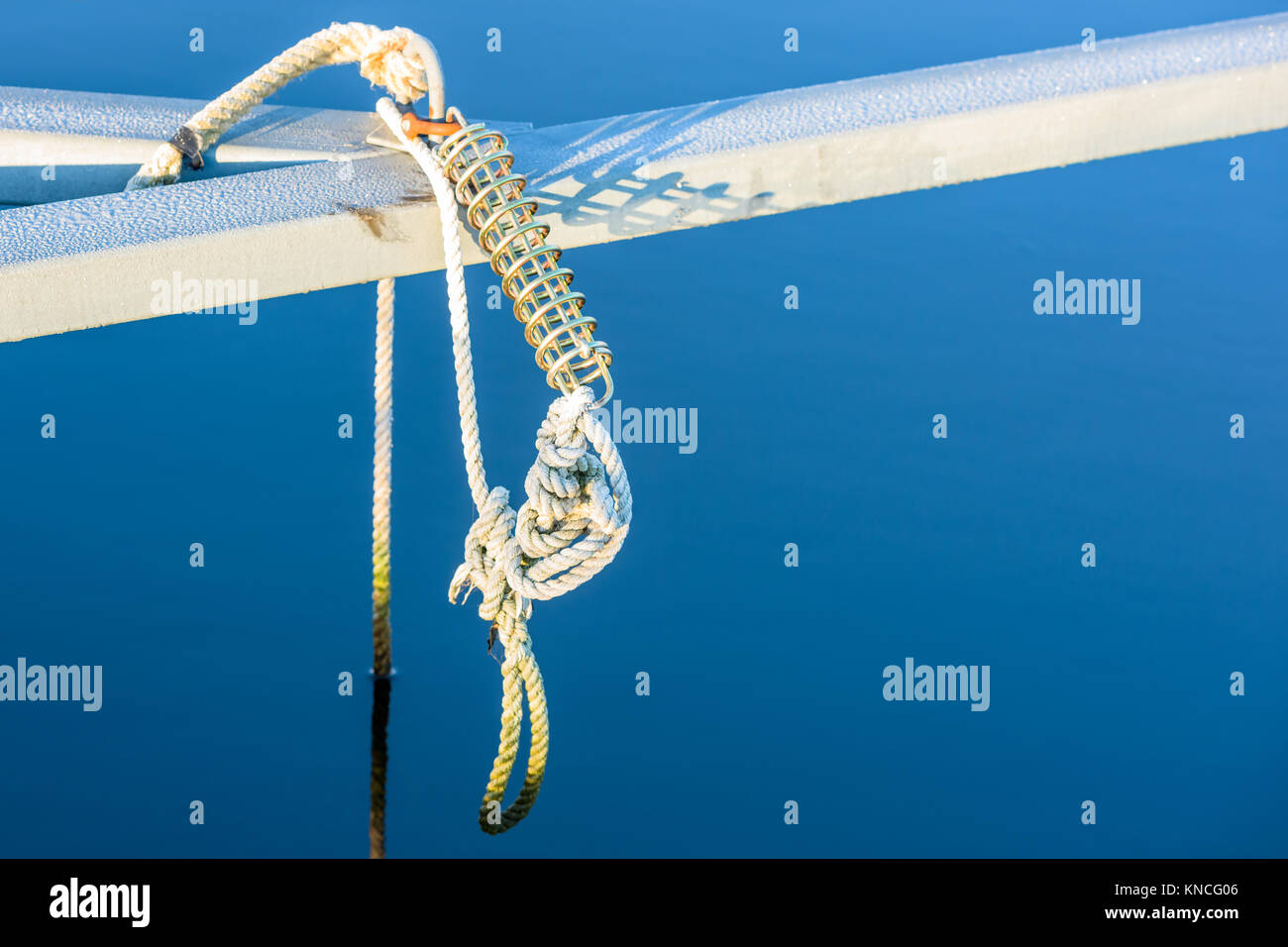 Mooring spring hanging with white rope from a marina with clear blue water in background. Frost on metal beam after a cold morning. Stock Photo