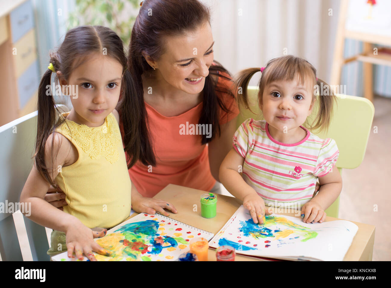 Mother and daughters are painting together. Happy family are coloring with paintbrush. Woman and children have a fun pastime. Stock Photo
