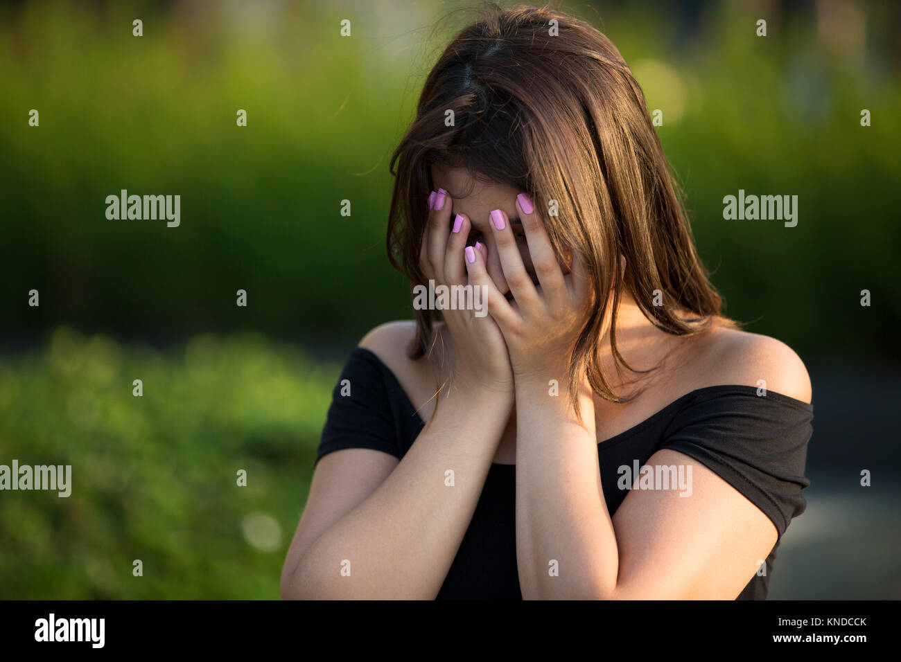 Young woman hiding face with hands outdoors crying Stock Photo
