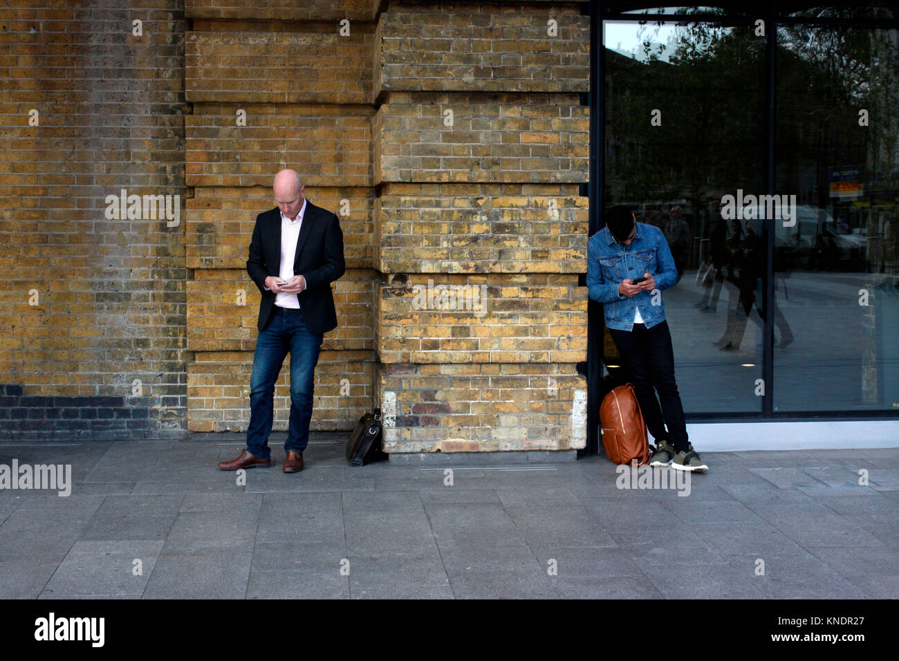 Two men both using their mobile phones outside Kings Cross train