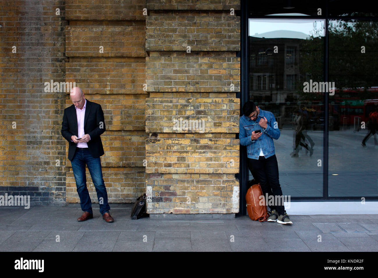 Two men both using their mobile phones outside Kings Cross train