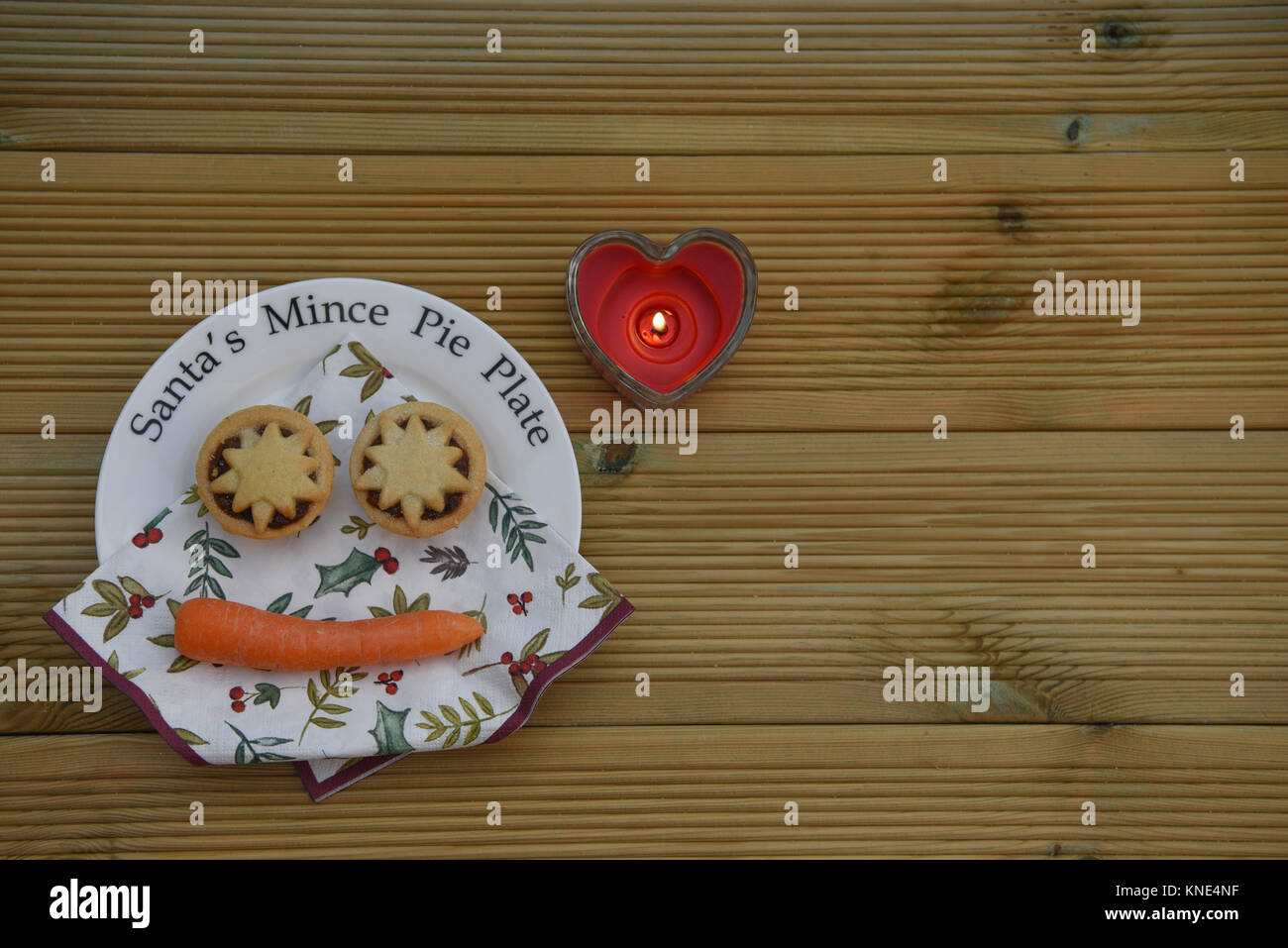 Christmas food photography image with Santa mince pie plate and orange carrot for the reindeer with love heart lit candle on wood background Stock Photo