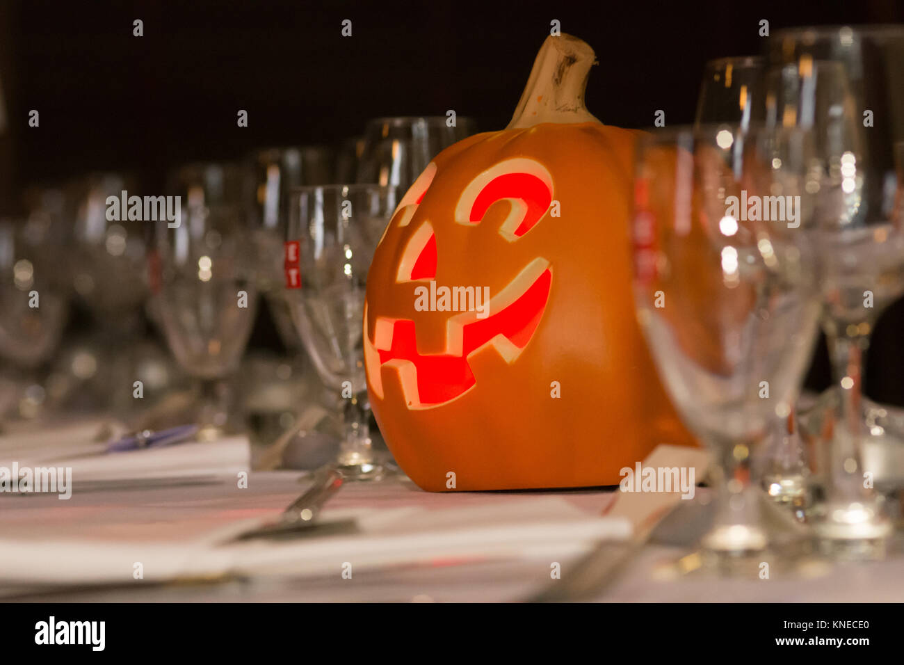 An illuminated artificial pumpkin sits among glasses at a themed wedding. Stock Photo