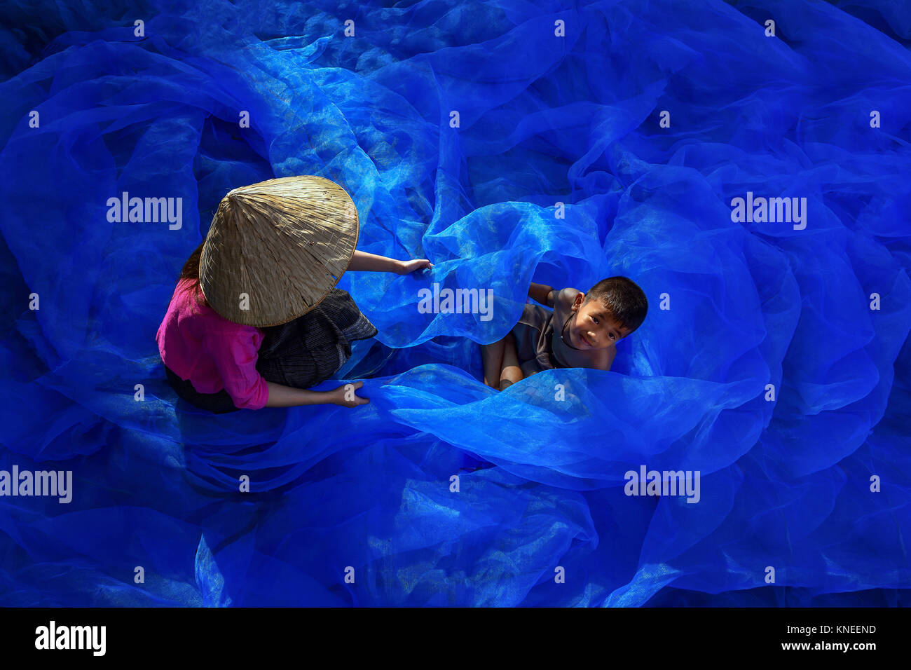Overhead view of a woman and boy repairing a fishing net, Thailand Stock Photo