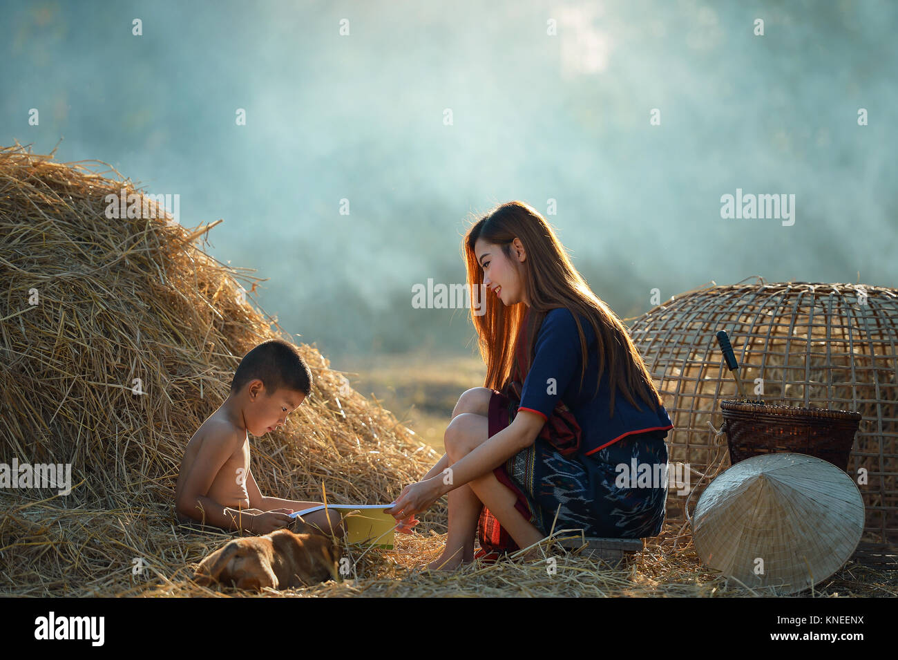 Woman and a boy reading a book together on a farm, Thailand Stock Photo