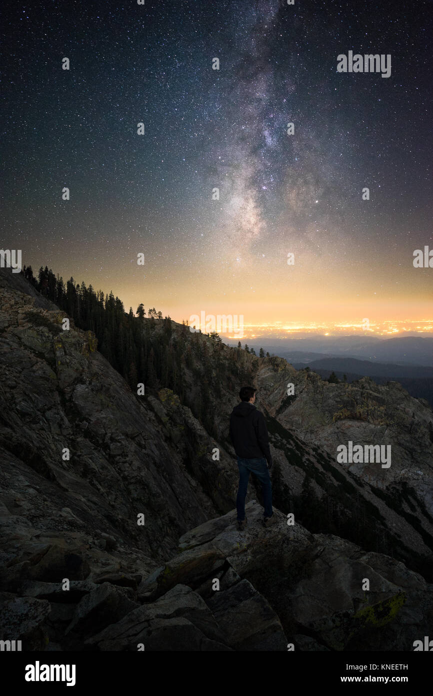 Man standing on Baldy Mountain looking at stars with Fresno in the distance, California, United States Stock Photo