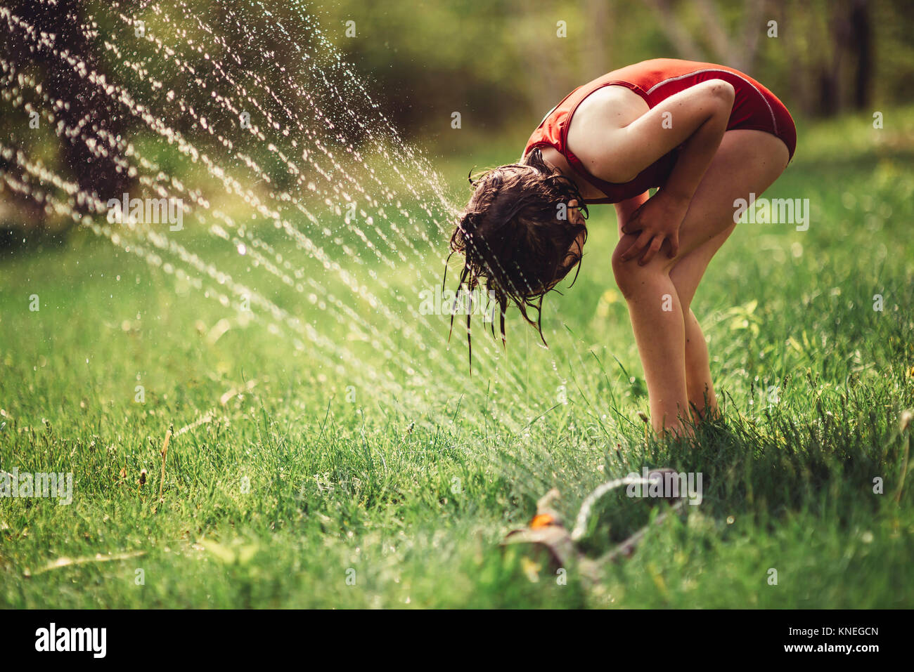 Girl playing in a sprinkler in the backyard Stock Photo