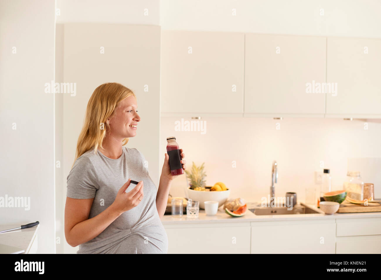 Pregnant young woman in kitchen with bottle of fruit juice Stock Photo