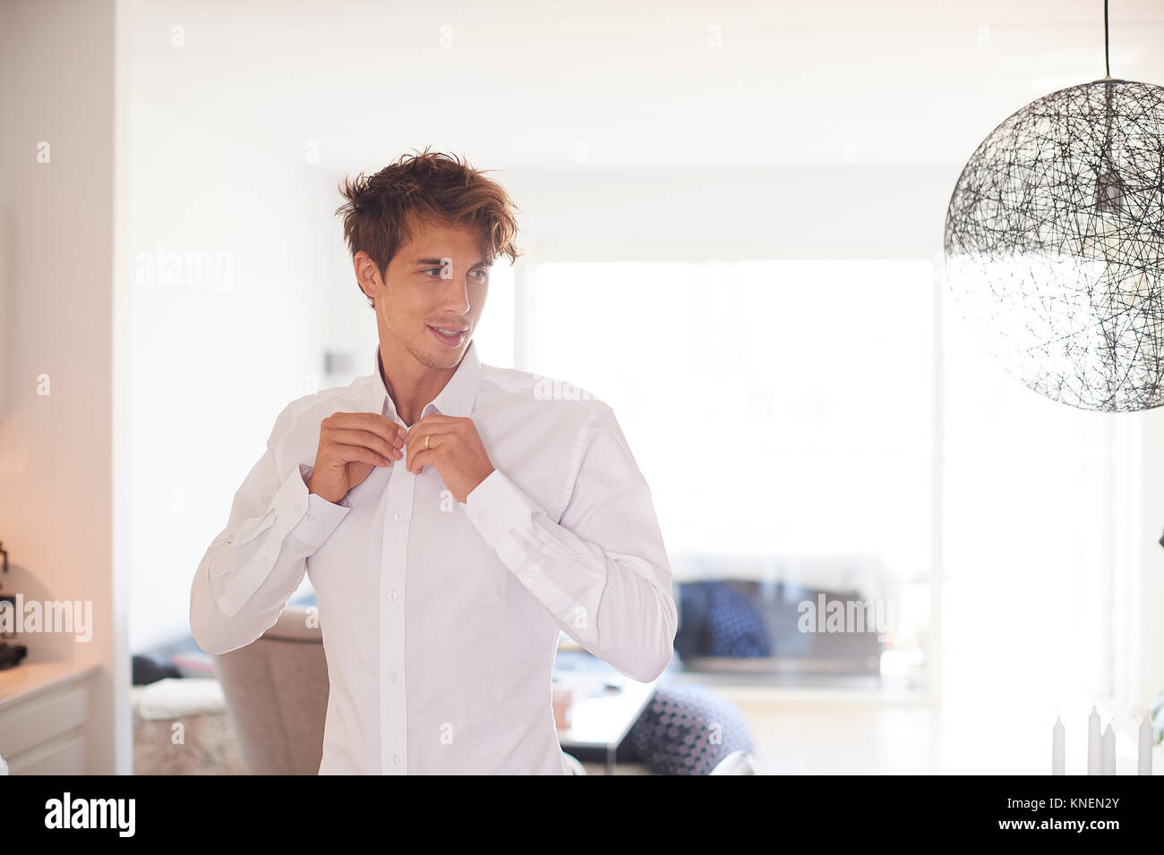 Mid adult man in living room buttoning shirt Stock Photo