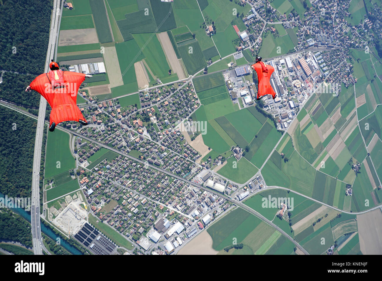 Aerial view of two wingsuit flyers in red suits flying above landscape Stock Photo