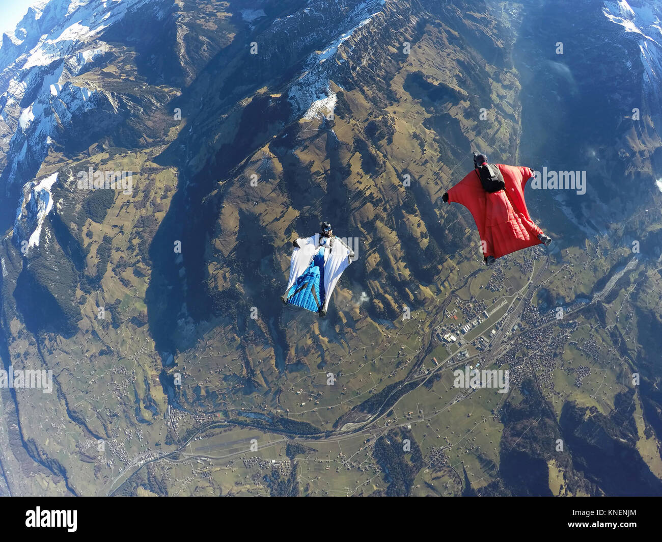 Aerial view of two wingsuit flyers, one on his back facing one in red suit flying above landscape Stock Photo