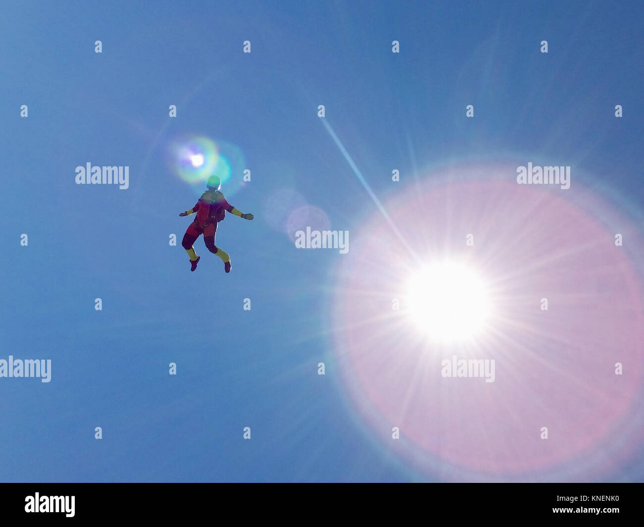 Female skydiver free falling upright against sunlit blue sky Stock Photo