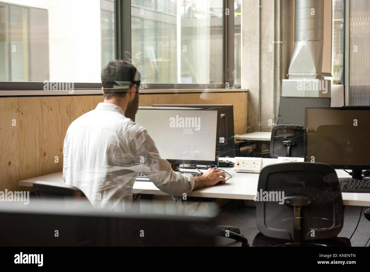 Rear view of man in office using desktop computer Stock Photo