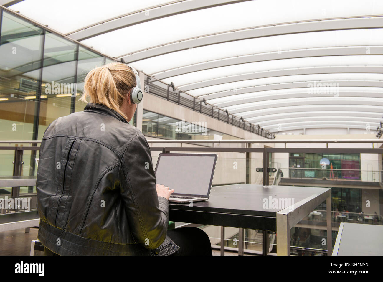 Rear view of woman on mezzanine of office building using laptop Stock Photo