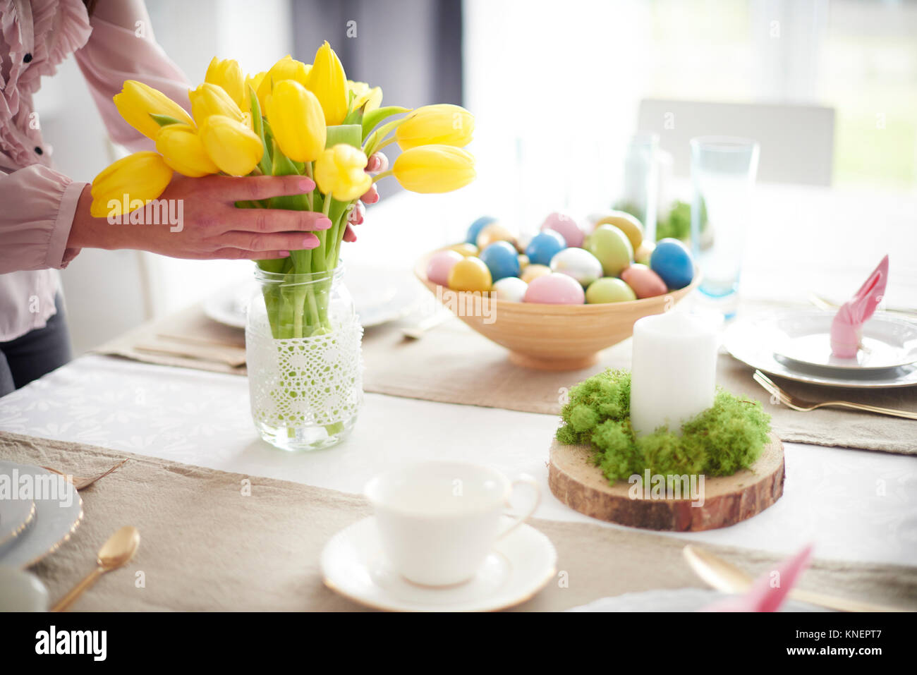 Hands of woman arranging yellow tulips at easter dining table Stock Photo