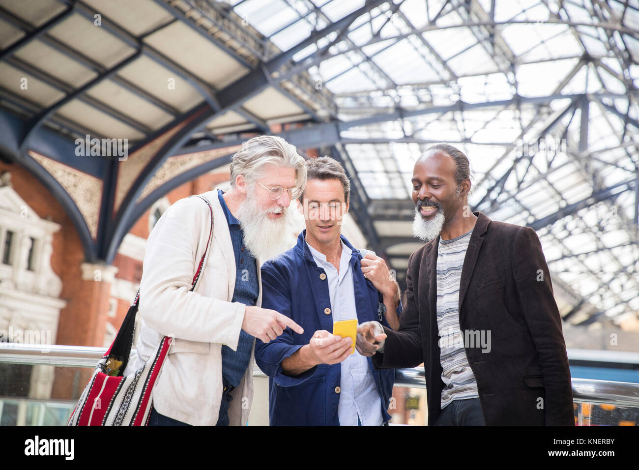 Three mature men at train station, looking at smartphone Stock Photo