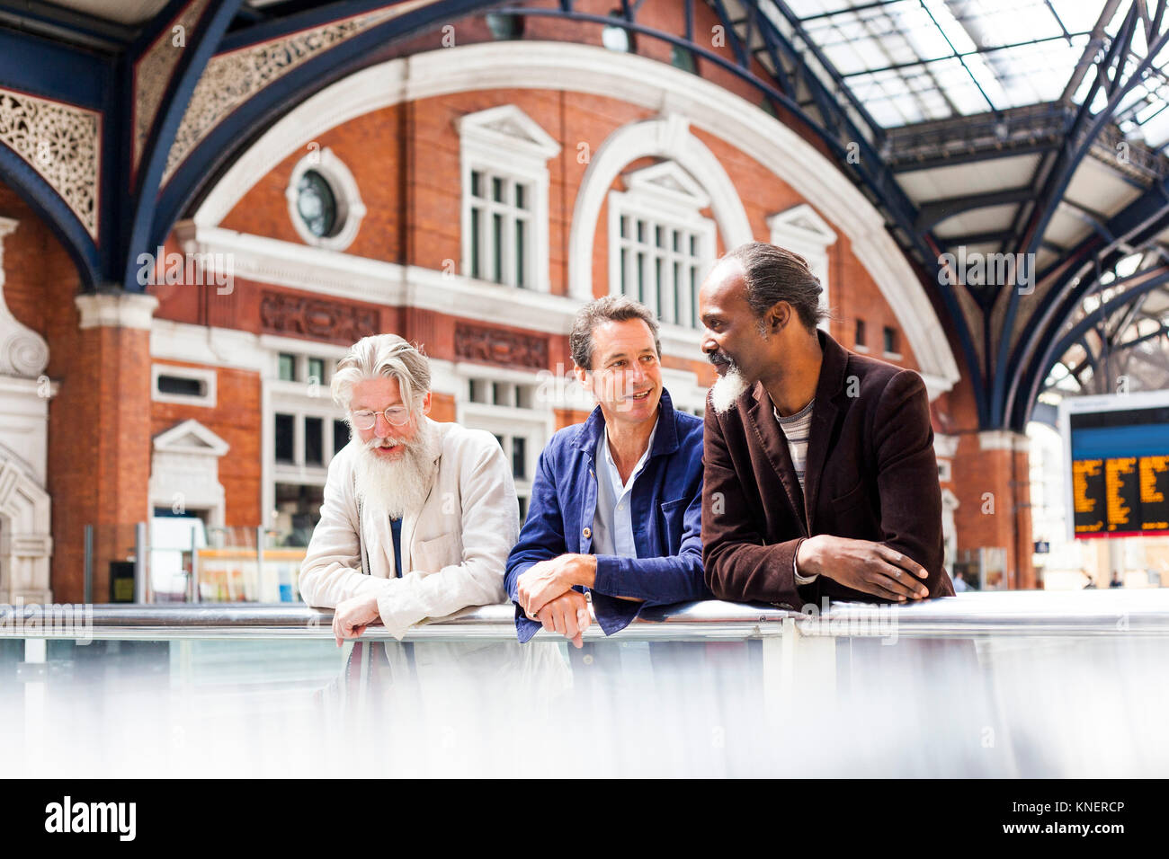 Three mature men at train station, standing together, talking Stock Photo