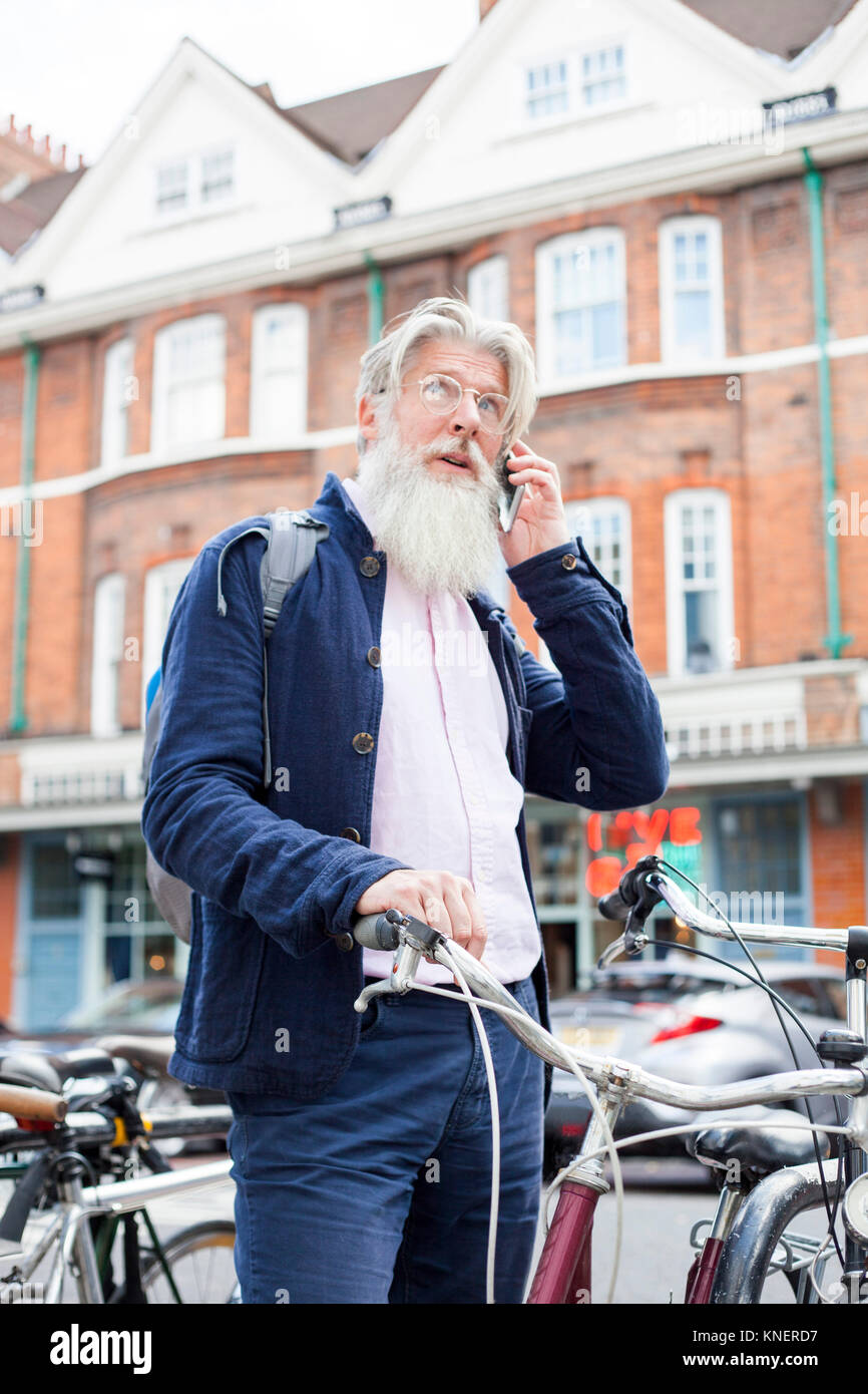 Mature man standing beside bicycle, using smartphone Stock Photo