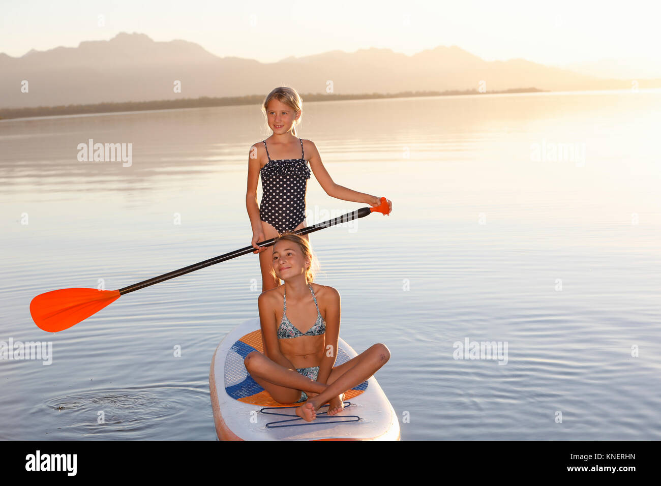 Two young girls paddle boarding on water Stock Photo