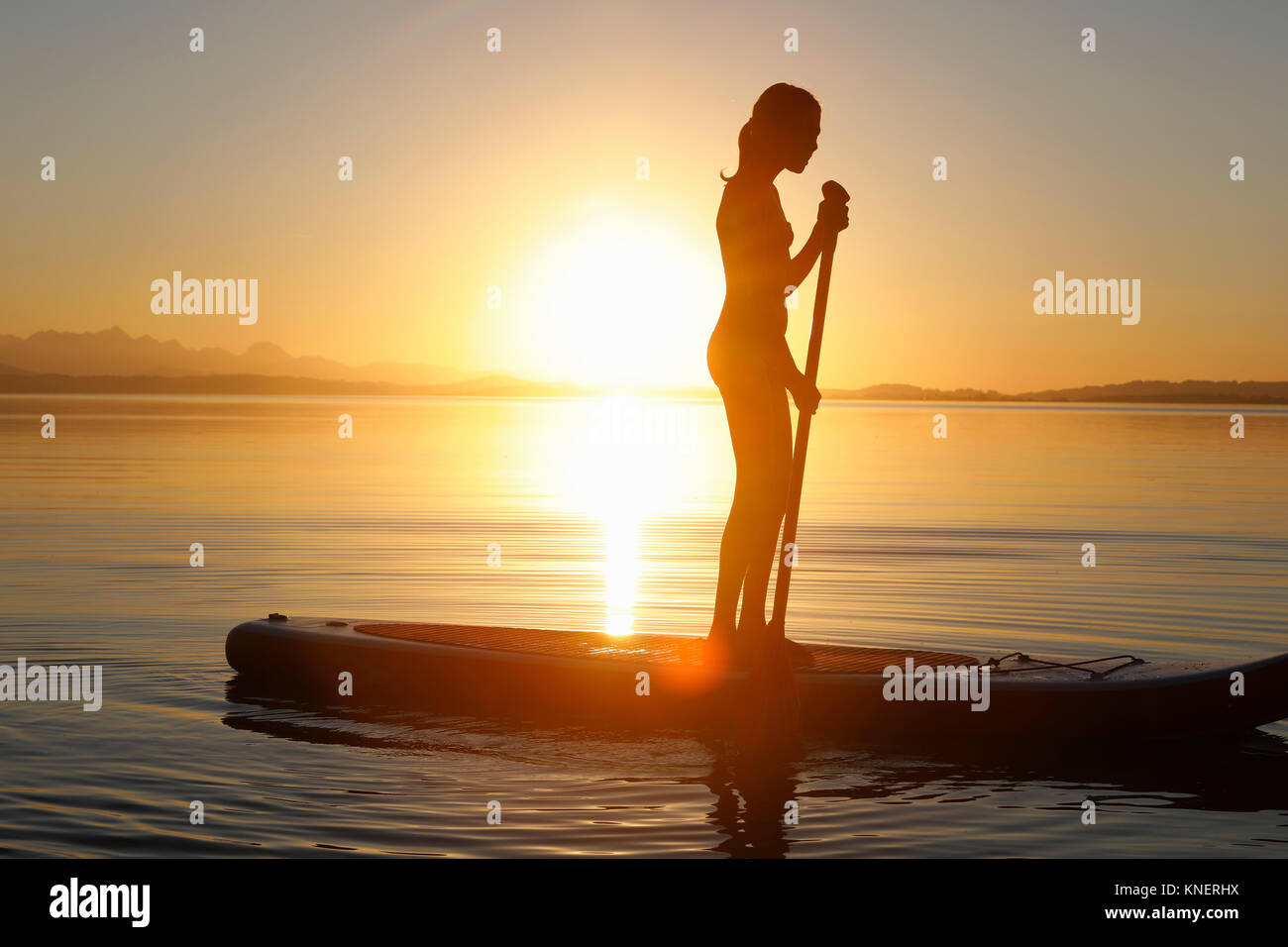 Young girl paddle boarding on water, at sunset Stock Photo