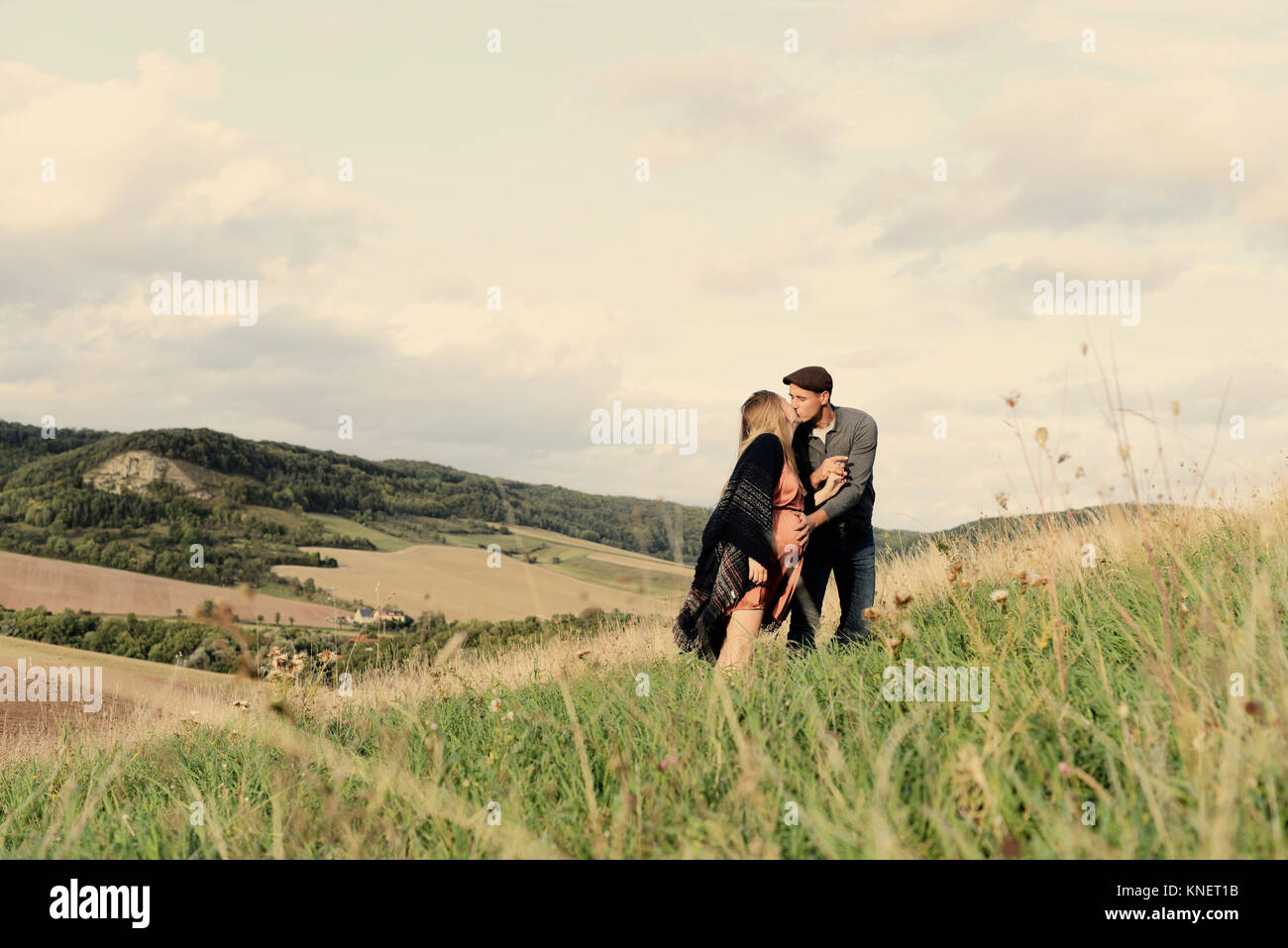 Romantic pregnant mid adult couple kissing on rural hillside Stock Photo