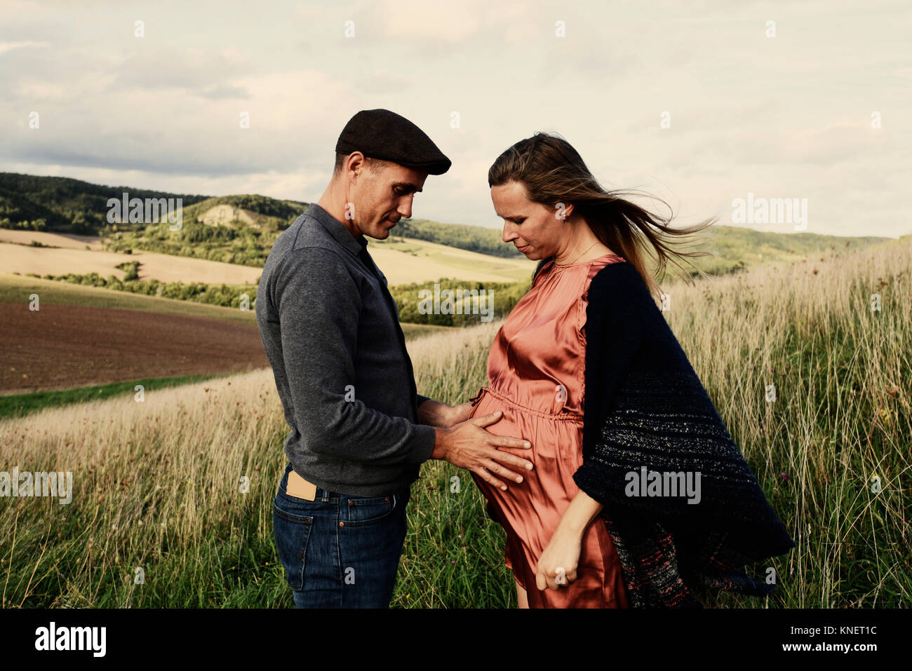 Romantic man with hands on pregnant wife's stomach on hillside Stock Photo