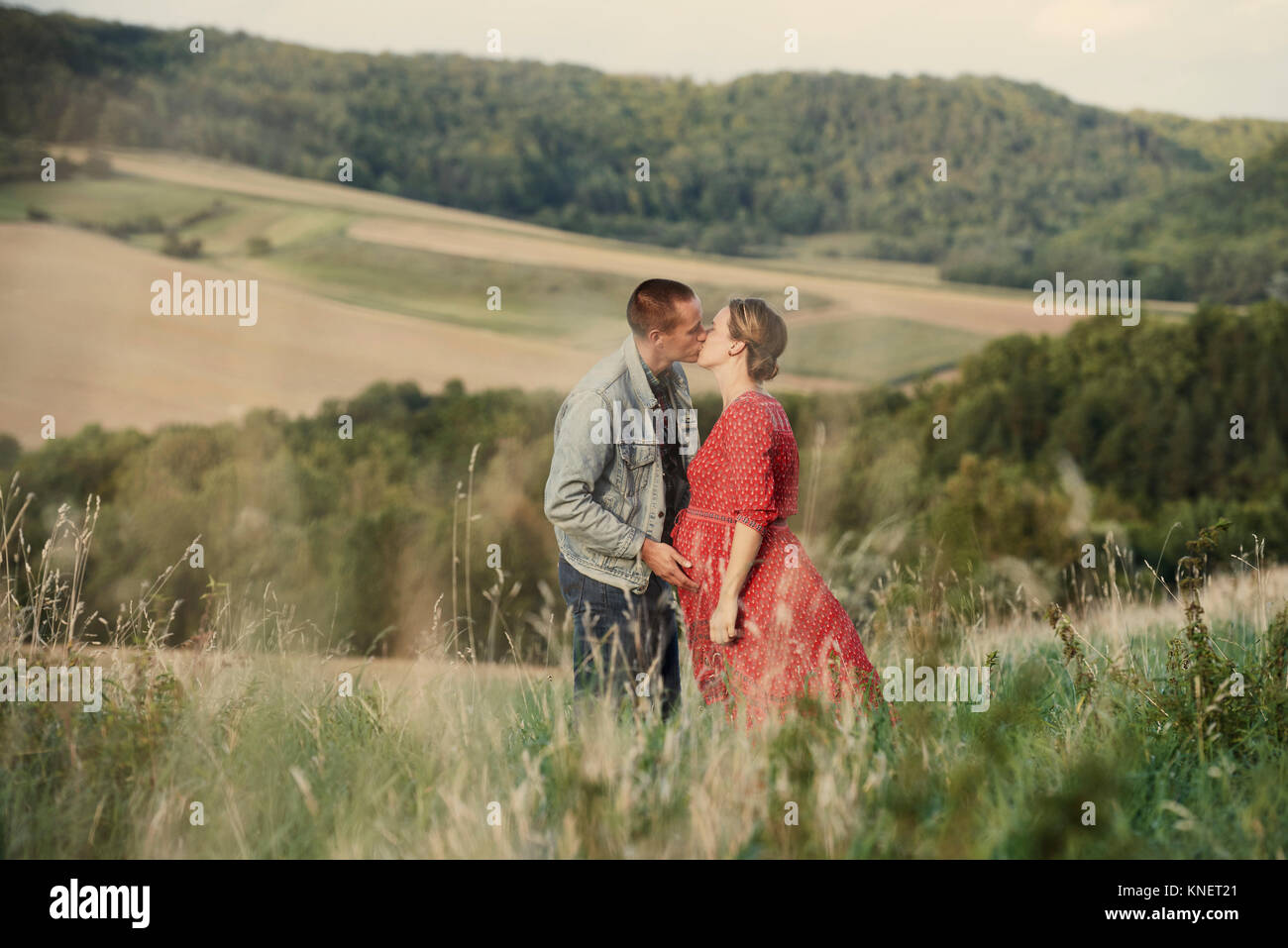 Romantic pregnant mid adult couple kissing in field Stock Photo