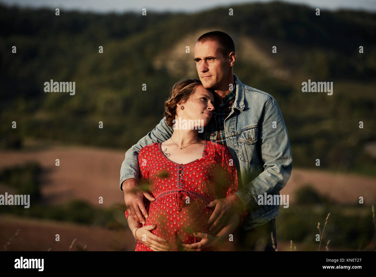 Romantic man with hands on pregnant wife's stomach in landscape Stock Photo