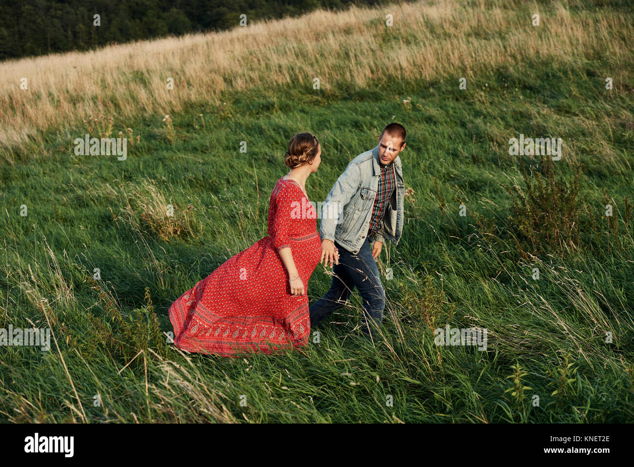 Pregnant couple strolling hand in hand in field Stock Photo