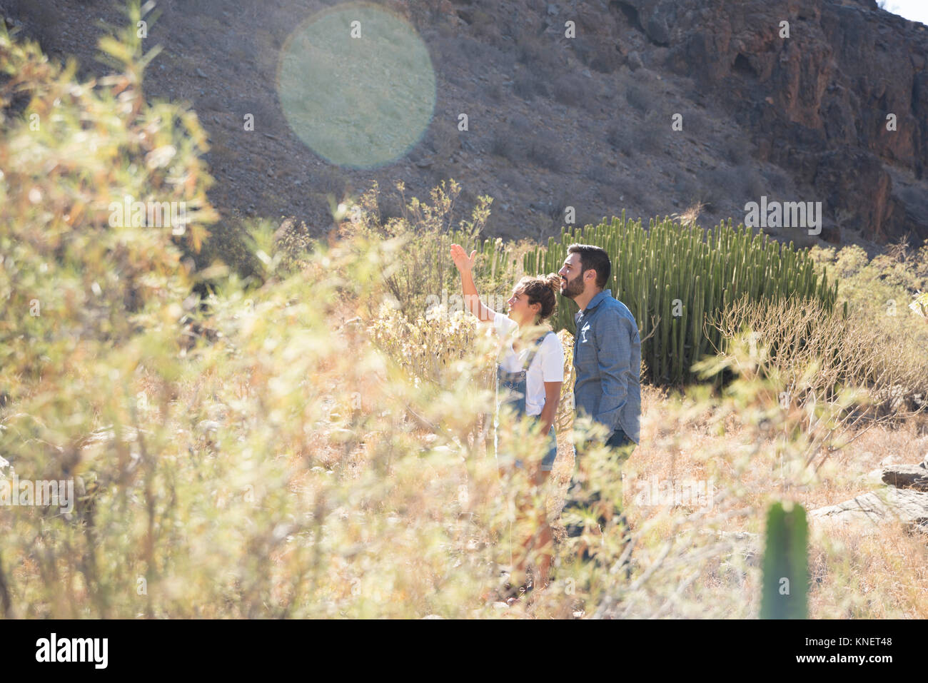 Young hiking couple looking up and pointing from sunlit valley, Las Palmas, Canary Islands, Spain Stock Photo