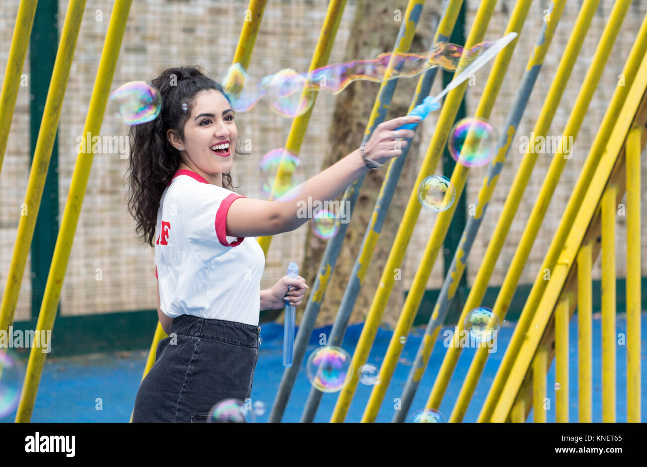 Enthusiastic young woman in playground making bubbles with bubble wand Stock Photo