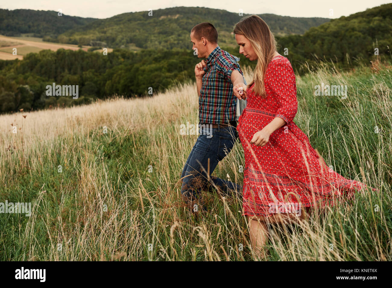 Pregnant mid adult couple holding hands while strolling down hillside Stock Photo