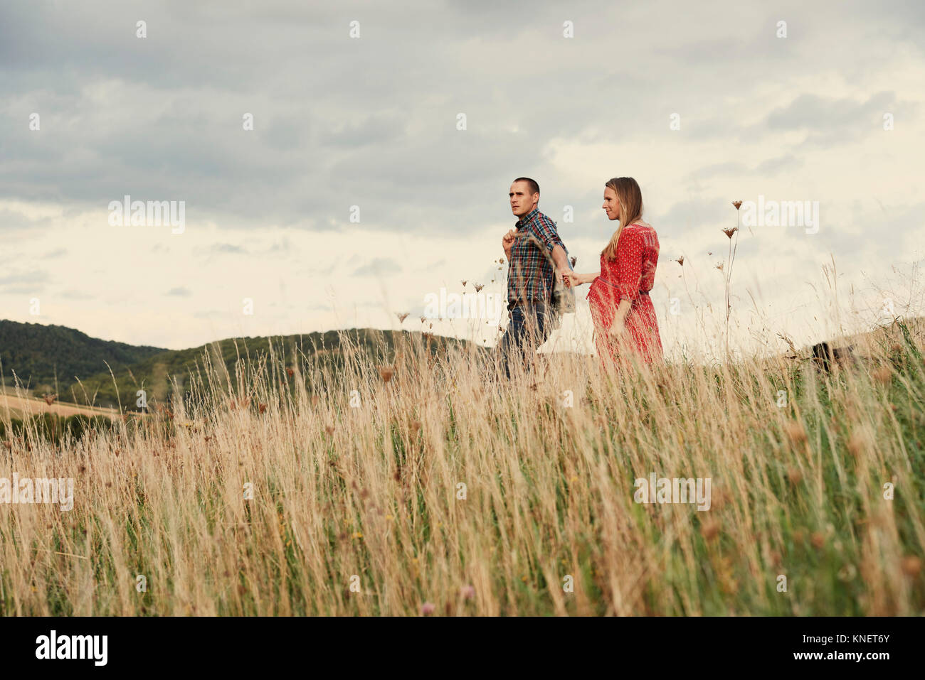 Pregnant mid adult couple holding hands while strolling down hillside Stock Photo