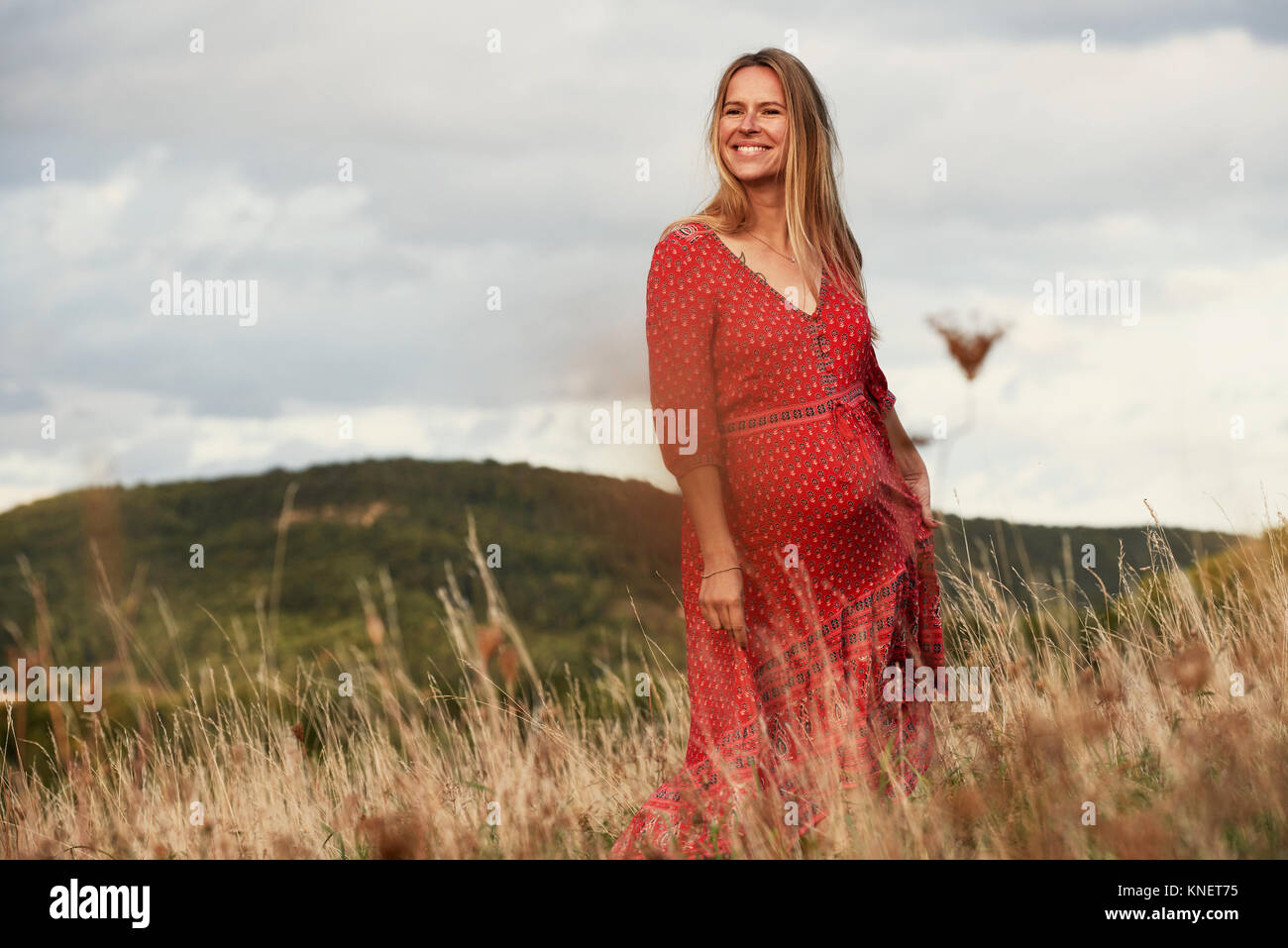 Portrait of happy pregnant woman in red dress on hillside Stock Photo