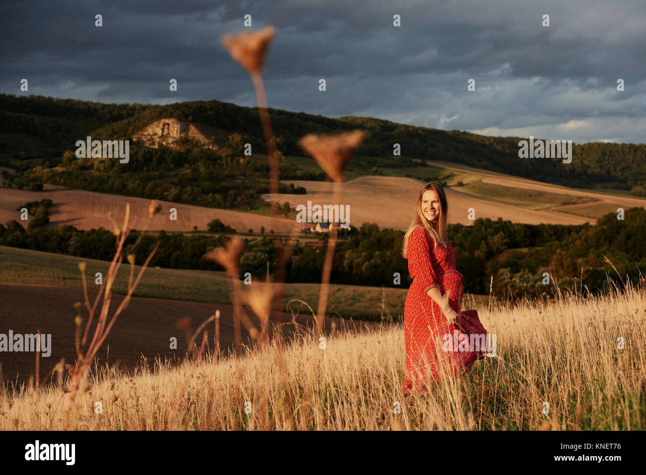 Portrait of happy pregnant woman in red dress on hillside Stock Photo