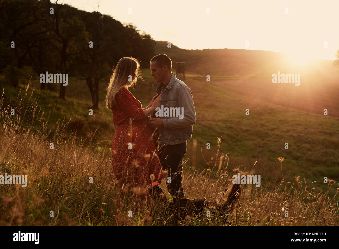 Romantic mid adult pregnant couple face to face on hillside at sunset Stock Photo
