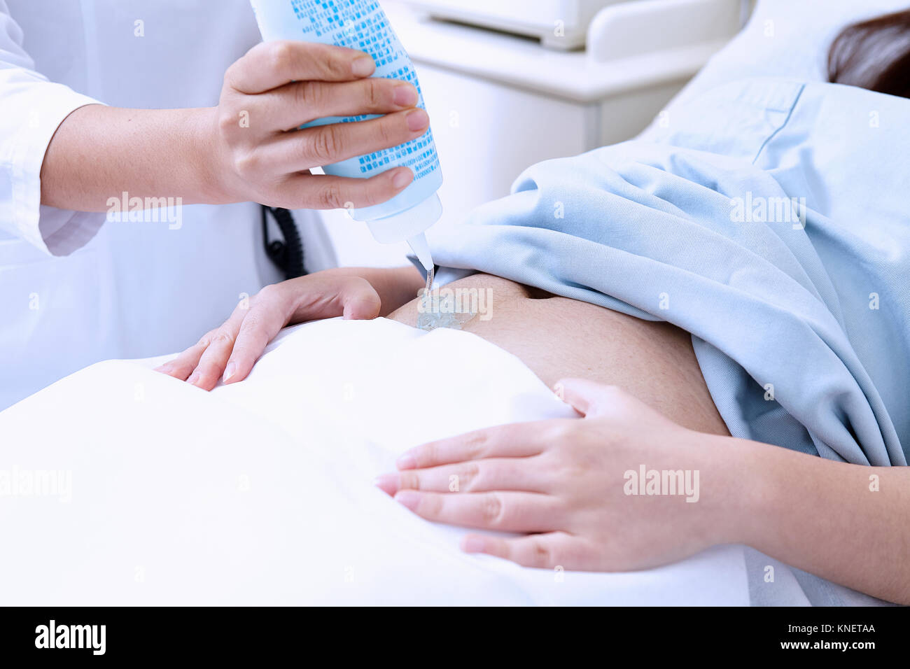 Cropped view of sonographer applying gel to pregnant patient stomach