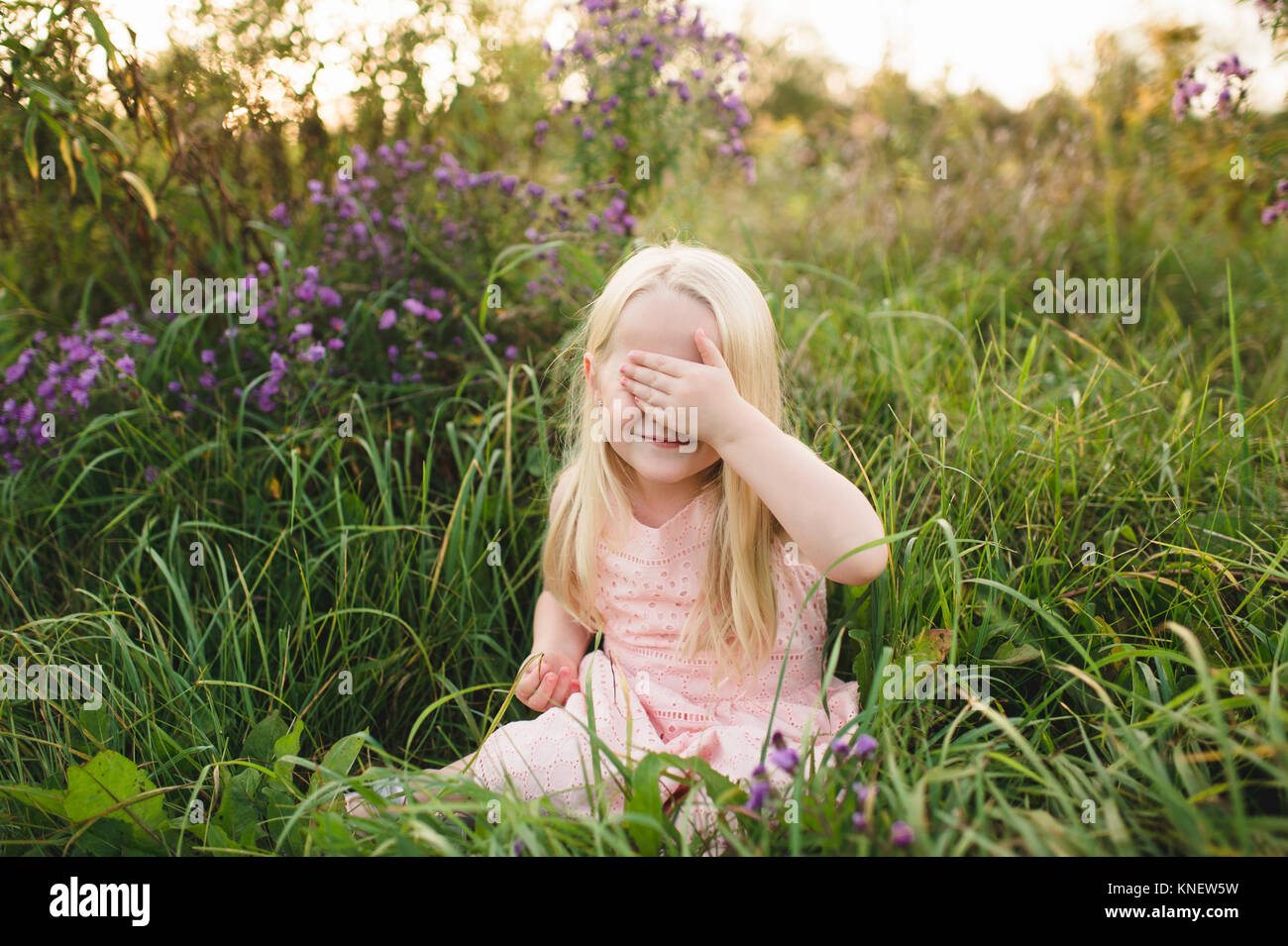 Girl sitting in tall grass, hand covering eyes Stock Photo
