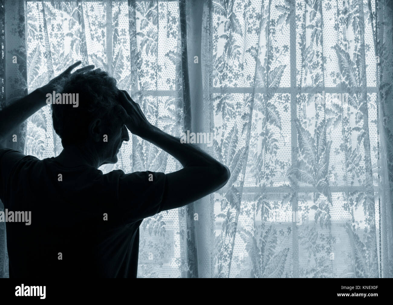Mature man with hand on head near window. Concept image for depression, male depression, mental health, male suicide... Stock Photo