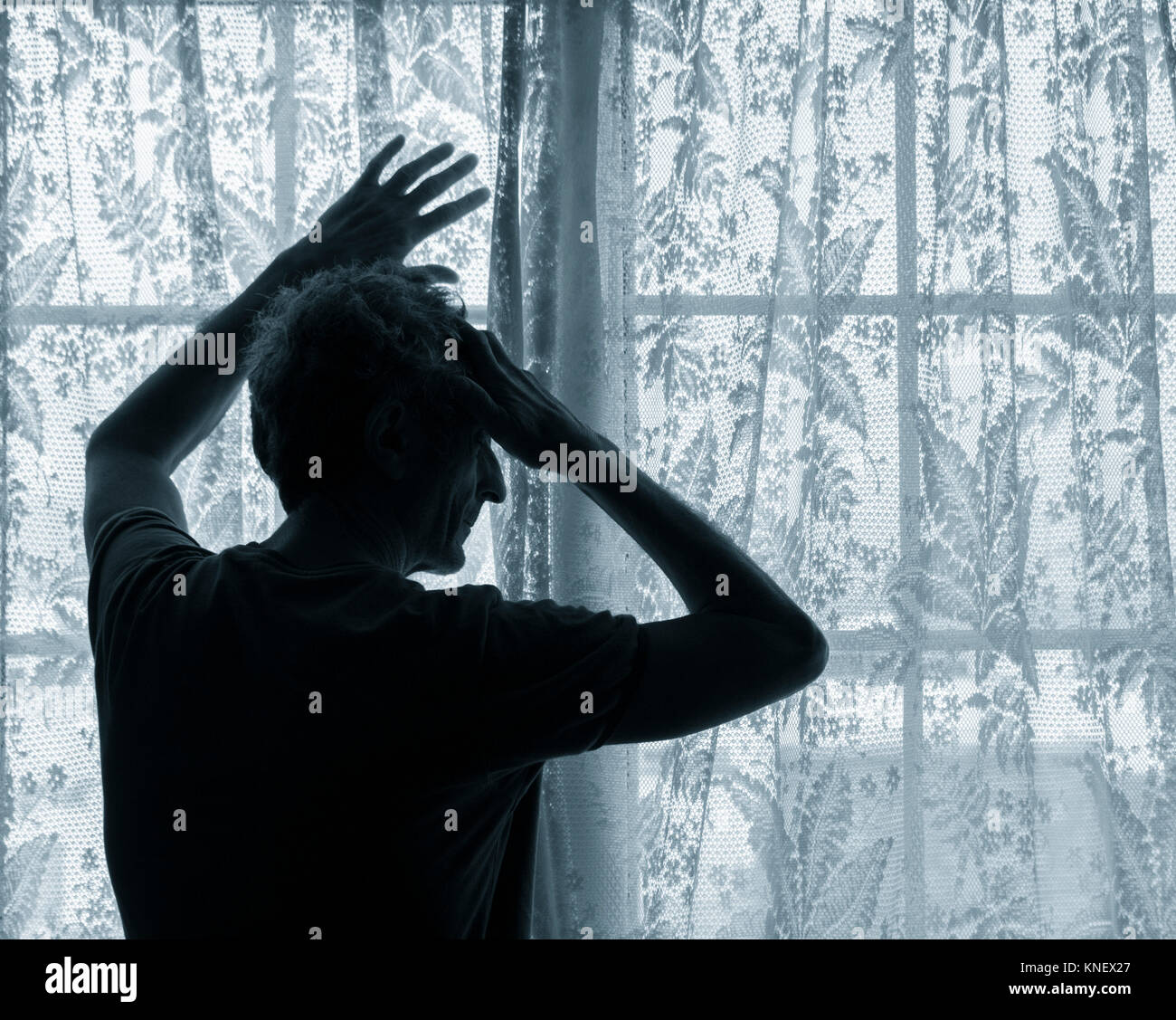 Mature man with hand on head near window. Concept image for depression, male depression, mental health, male suicide... Stock Photo