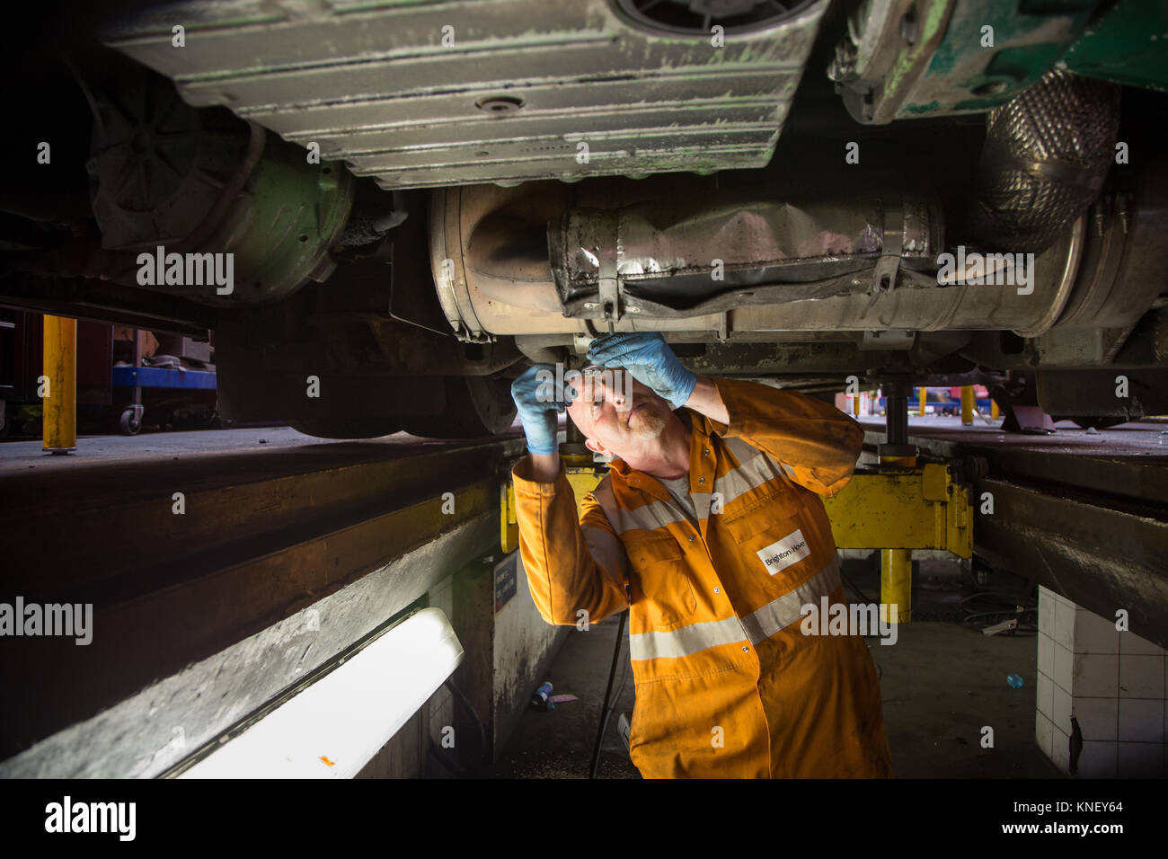 A mechanic working on the engine of a bus from underneath, at the Brighton and Hove Bus Depot Stock Photo