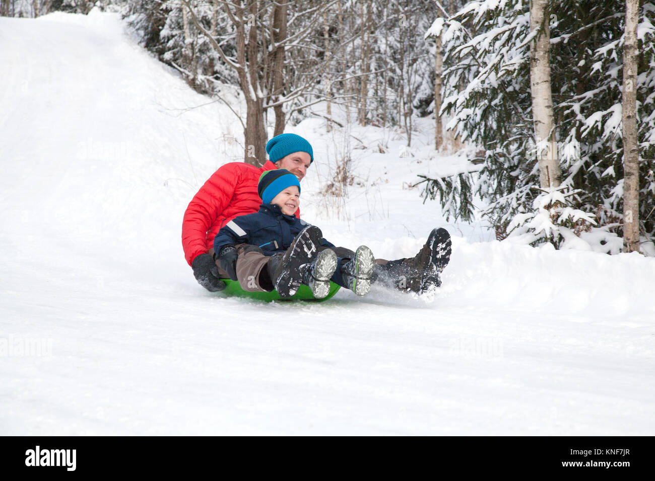 Man and son tobogganing down hill in snow covered forest Stock Photo