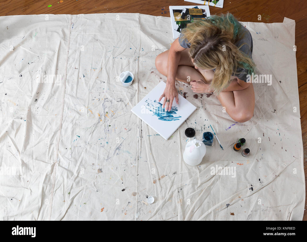 Overhead view of female artist sitting on dust sheet finger painting abstract canvas Stock Photo