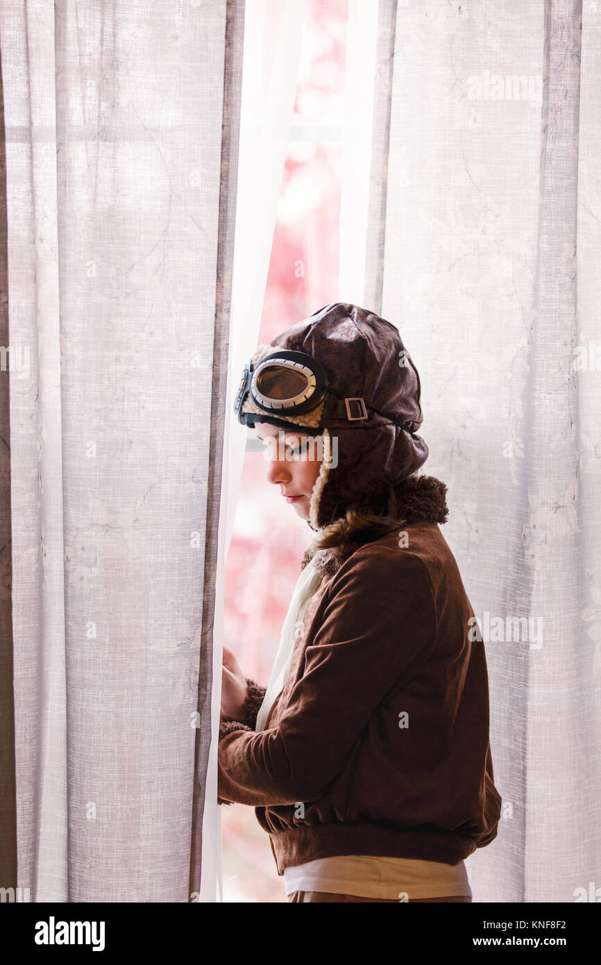 Girl looking out through window wearing pilot costume for halloween Stock Photo