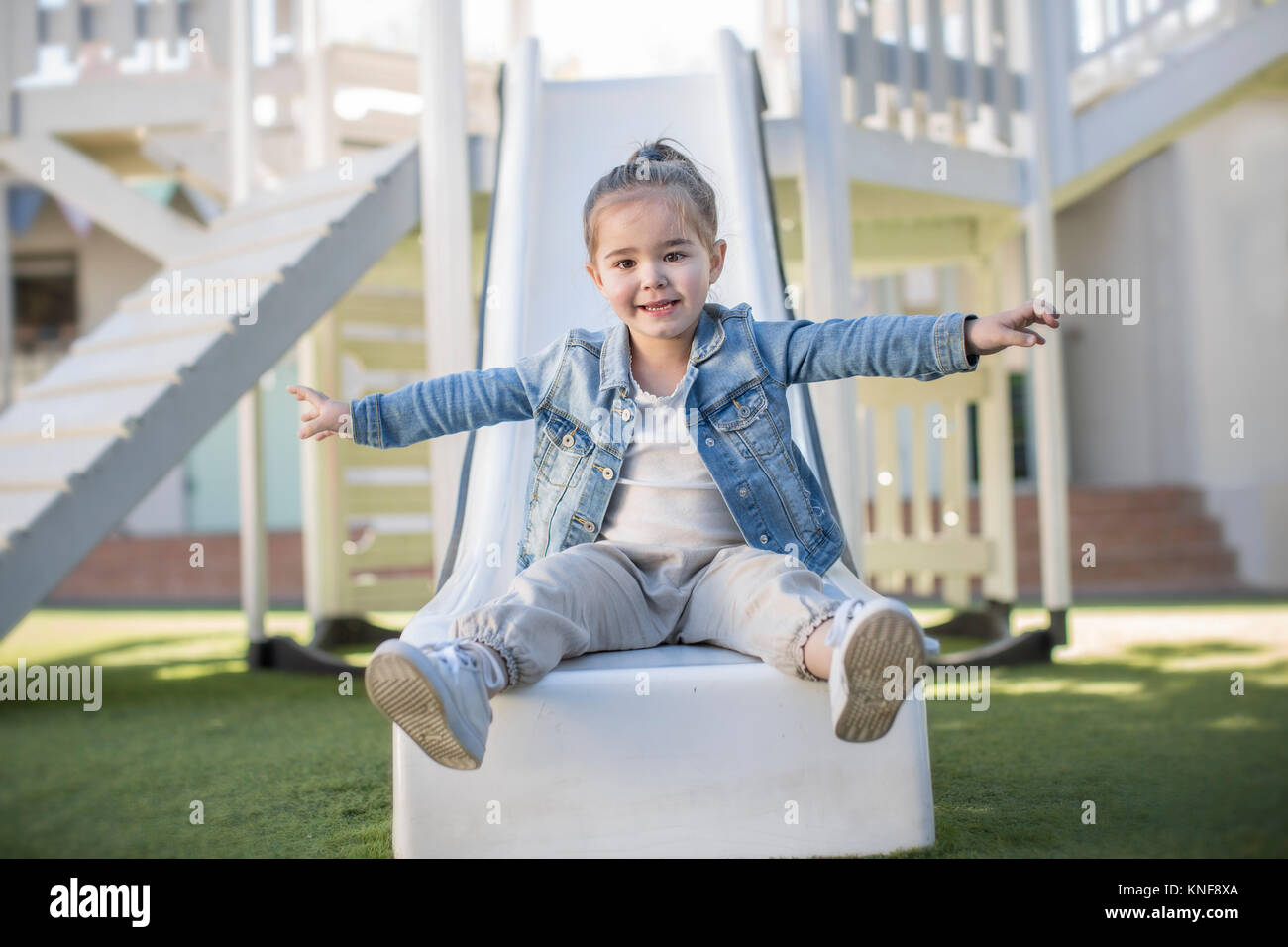 Girl at preschool, portrait sitting on playground slide in garden Stock ...