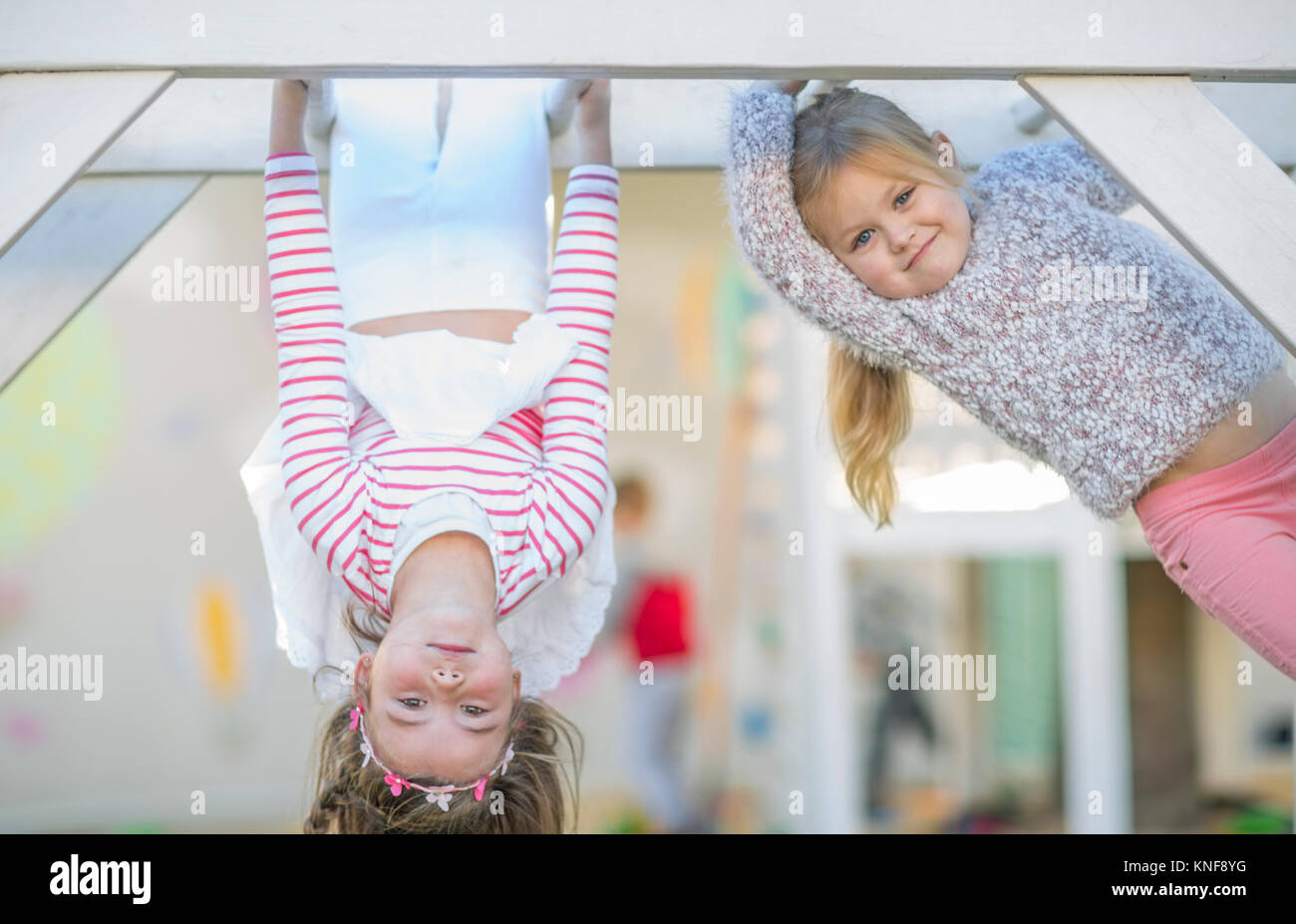 Girls at preschool, portrait climbing and upside down on climbing frame in garden Stock Photo