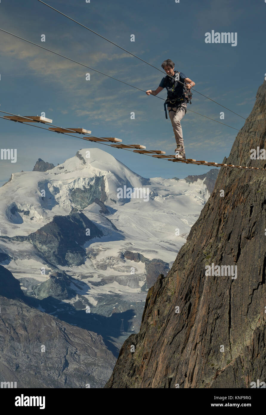 Mature male climber stepping across wire rope bridge, Jegihorn, Valais, Switzerland Stock Photo