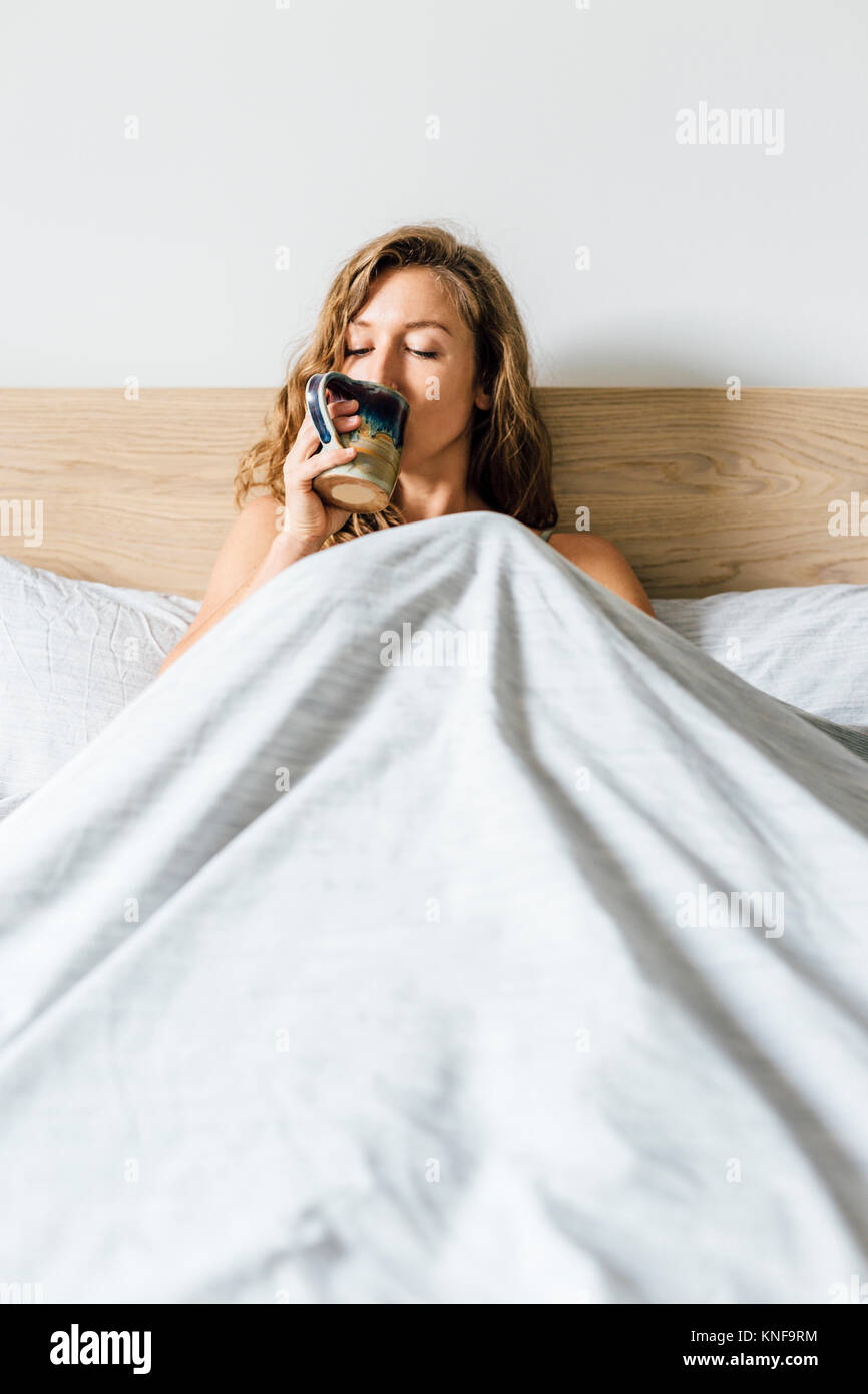 Young woman sitting up in bed drinking coffee Stock Photo Alamy