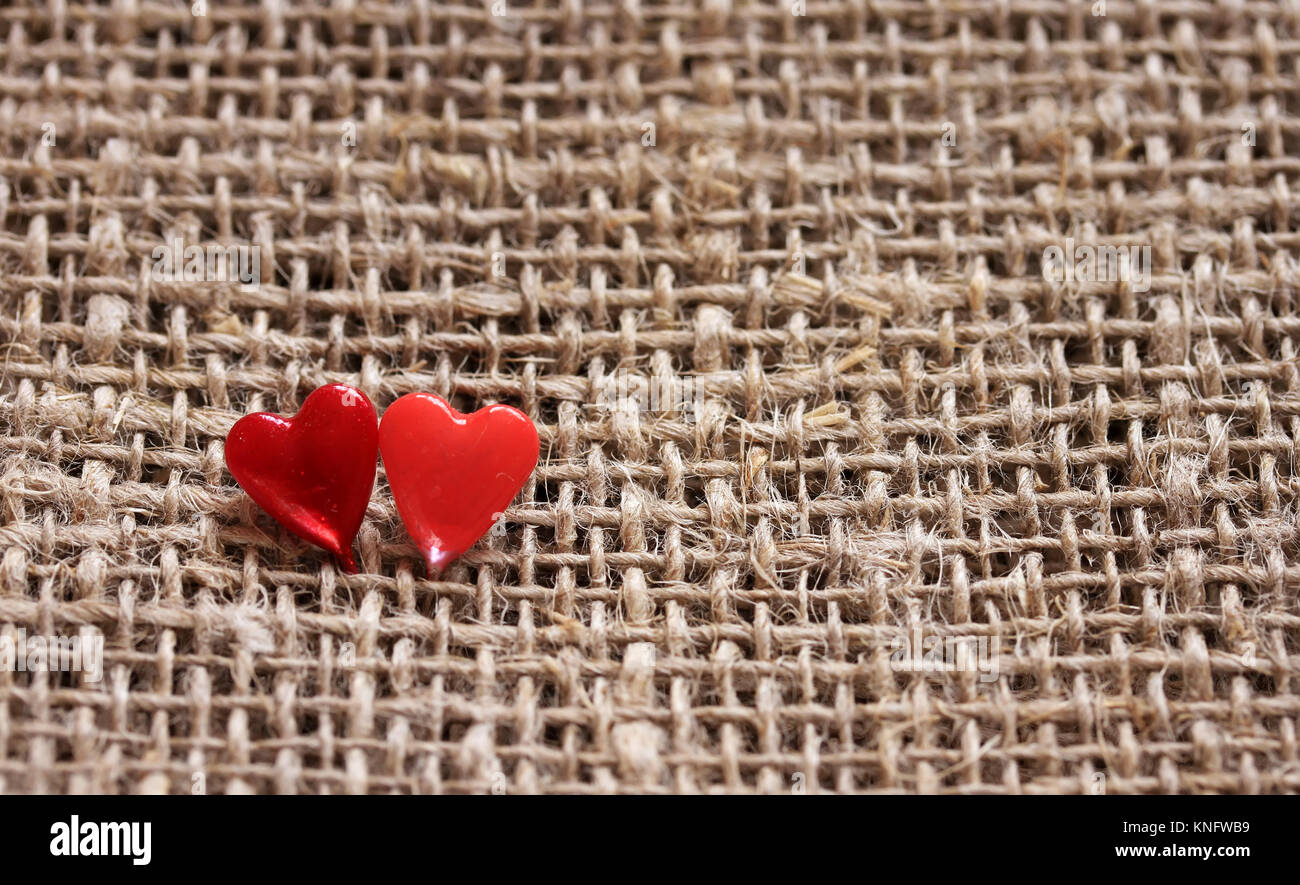 a pair of sharp pins in the form of red hearts stuck in the rough burlap Stock Photo